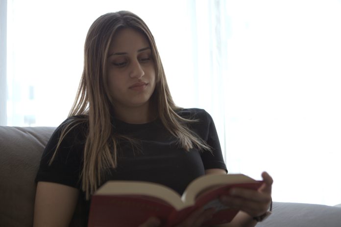 Young girl reading a book on the couch at home.