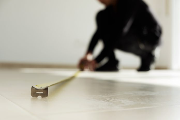 man using a measuring tape on a tiled floor