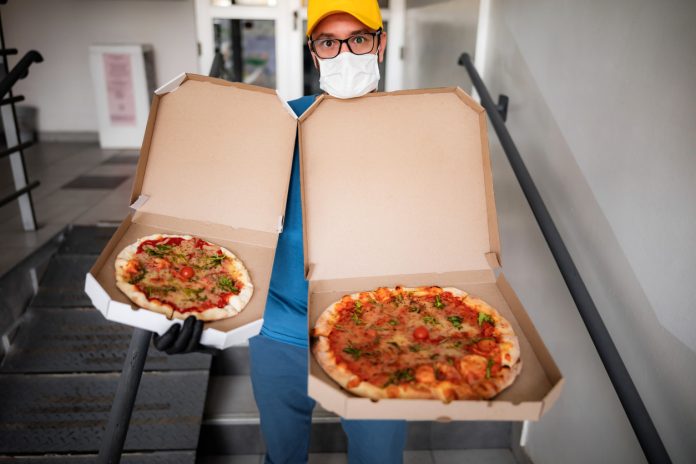 Deliveryman with protective medical mask holding pizza box - days of viruses and pandemic, food delivery to your home.