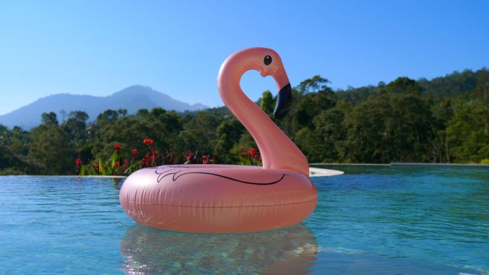 The hottest summer swimming accessory is the pink flamingo. An inflatable toy floats in a private pool in clear clear water in a tropical villa. The concept of vacation in an exotic country.
