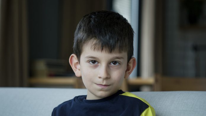 A young boy sits on a couch, looking warmly at the camera. Close-up portrait of joy and innocence of childhood in a cozy home