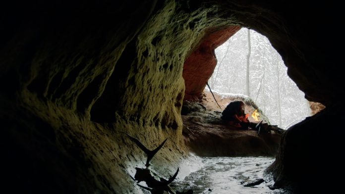 Wild caveman sitting near bonfire in dark cave