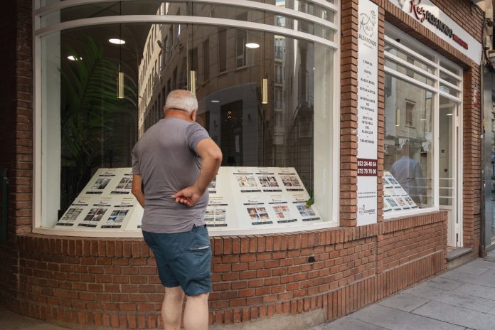 Man Looking at Property Listings in Real Estate Office Window on Urban Street in Salamanca, Spain